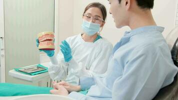Asian female dentist explaining orthodontic care and whitening to young male patient with teeth model in dental clinic, well-being hygiene, and professional healthcare work in doctor office hospital. video