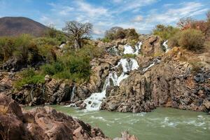 a waterfall in the desert with rocks and trees photo