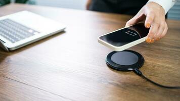 Charging mobile phone battery with wireless charging device in the table. Smartphone charging on a charging pad. Mobile phone near wireless charger Modern lifestyle technology concept. photo