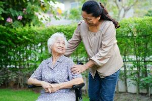 Caregiver help Asian elderly woman disability patient sitting on wheelchair in park, medical concept. photo