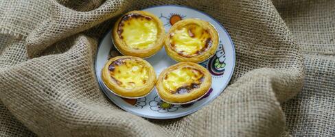 Small egg tarts on a round plate, dessert. on brown fabric background. Wallpaper photo