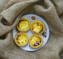 Homemade small egg tarts on a round plate, dessert. on brown fabric background photo