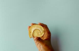 Young asian women pick mini vanilla roll cake, swiss roll cake or sponge roll with Vanilla flavor. Thai call Jam Rolls. isolated on blue background photo