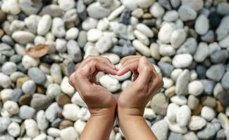 Female hand making heart symbol, blurred stones as background. Love concept on Valentine day. photo