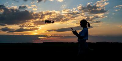 silhouette of woman controlling drone on sunset background photo