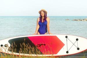 Sup boarding. A woman in a hat poses standing with a sup board. The concept of active lifestyle and surfing. photo