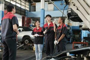 masculino experto supervisor ingeniero tren y discutir con profesional mecánico trabajador equipos, inspeccionar reparar trabajo a coche Servicio cochera, armonioso grupo, y hacer mantenimiento trabajos en automotor industria. foto