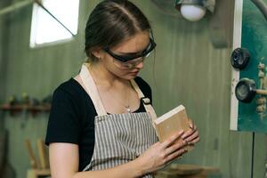 Hardworking carpenter woman using tools smiling confidently young female joiner in apron standing near workbench working in the craft workshop photo