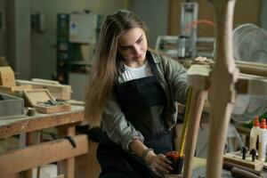 Young beautiful carpenter woman working with wood plank, a female craft worker making wooden furniture in a woodworking workshop. photo