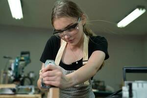 joven hermosa carpintero mujer trabajando con madera tablón, un hembra arte trabajador haciendo de madera mueble en un carpintería taller. foto