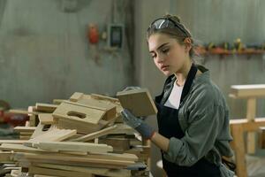 Hardworking carpenter woman using tools smiling confidently young female joiner in apron standing near workbench working in the craft workshop photo