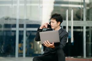 Young Asian business man working at outside business center with laptop, tablet, smartphone  and taking notes on the paper. photo