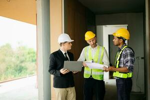 Contractor and architect looking at plan, tablet, laptop and talking about working on big project. Building in construction process photo