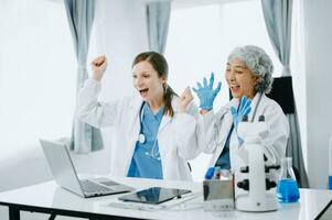 Medical team having a meeting with doctors in white lab coats and surgical scrubs seated at a table discussing a patients working online using computers in the medical industry photo