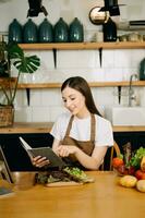 Young beautiful woman in the kitchen in an apron, fresh vegetables on the table, writes down her favorite recipes, comes up with ideas for dishes photo