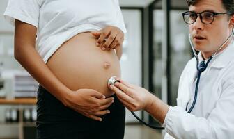 Pregnant african woman has appointment with doctor at clinic. Male gynaecologist OB GYN medic specialist with stethoscope listens to baby's heartbeat in mother's belly. Pregnancy, health care photo