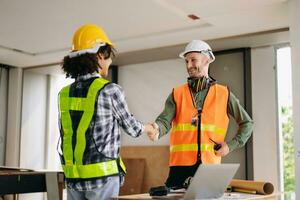Construction team shake hands greeting start new project plan behind yellow helmet on desk in office center to consults about their building project. photo