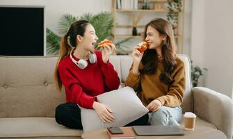 dos asiático belleza sonriente joven mujer sentado en sofá atractivo casual niña sensación contento y relajarse, tener divertido reloj comedia vídeo en televisión en casa. actividad estilos de vida concepto foto