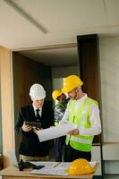 Contractor and architect looking at plan, tablet, laptop and talking about working on big project. Building in construction process photo