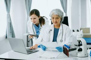 Medical team having a meeting with doctors in white lab coats and surgical scrubs seated at a table discussing a patients working online using computers in the medical industry.. photo