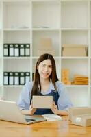 Asian young woman SME working using smartphone or tablet taking receive and checking online purchase shopping order photo