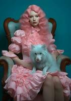 A girl with beautiful wavy long hair in a romantic dress with ruffles and puff sleeves sits in a vintage armchair and holds a fluffy pastel pet photo