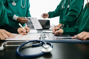 Medical team having a meeting with doctors in white lab coats and surgical scrubs seated at a table discussing a patients working online using computers in the medical industry photo
