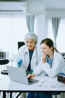 Medical team having a meeting with doctors in white lab coats and surgical scrubs seated at a table discussing a patients working online using computers in the medical industry photo