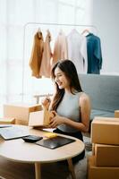 Startup small business SME, Entrepreneur owner woman using smartphone or tablet taking receive and checking online purchase shopping order to preparing pack product box. photo