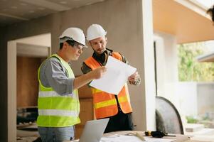 Contractor and architect looking at plan, tablet, laptop and talking about working on big project. Building in construction process interior. team work photo