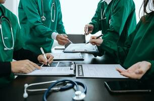 Medical team having a meeting with doctors in white lab coats and surgical scrubs seated at a table discussing a patients working online using computers in the medical industry photo