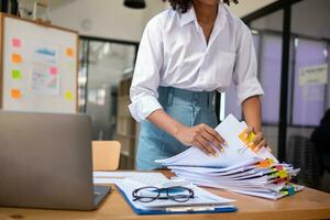 secretary searches through stacked documents on desk in office to find lease within stacked documents just before meeting. concept difficulty in finding hire purchase contract from stacked documents photo