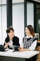 Two Asian business workers talking on the smartphone and using laptop at the modern office. photo