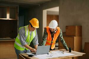 Contractor and architect looking at plan, tablet, laptop and talking about working on big project. Building in construction process interior. team work photo