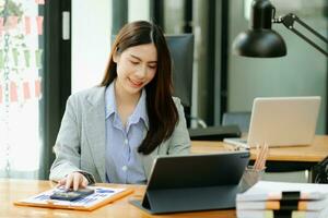 Asian woman with a smile standing holding notepad and tablet at the modern office. photo