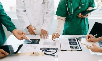 Medical team having a meeting with doctors in white lab coats and surgical scrubs seated at a desk discussing a patients working online using computers in the medical industry photo
