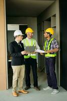 Contractor and architect looking at plan, tablet, laptop and talking about working on big project. Building in construction process photo