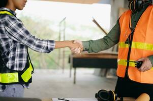 Construction team shake hands greeting start new project plan behind yellow helmet on desk in office center to consults about their building project. photo