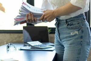 secretary searches through stacked paperwork on desk in office to find lease within stacked paperwork just before meeting. concept difficulty in finding hire purchase contract from stacked paperwork photo