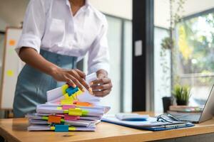 secretary searches through stacked documents on desk in office to find lease within stacked documents just before meeting. concept difficulty in finding hire purchase contract from stacked documents photo