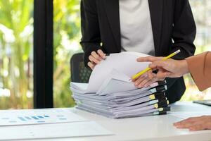 secretary searches through stacked paperwork on desk in office to find lease within stacked paperwork just before meeting. concept difficulty in finding hire purchase contract from stacked paperwork photo