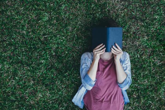 Young woman lying alone reading book on green lawn in  backyard and having copy space to put text on side on  green lawn The concept of reading books to learn and understand the articles in the book. photo