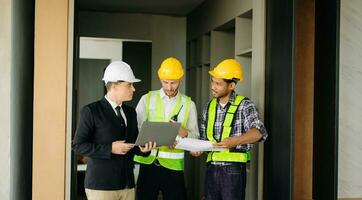 Contractor and architect looking at plan, tablet, laptop and talking about working on big project. Building in construction process photo