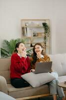 dos asiático belleza sonriente joven mujer sentado en sofá atractivo casual niña sensación contento y relajarse, tener divertido reloj comedia vídeo en televisión en casa. actividad estilos de vida concepto foto