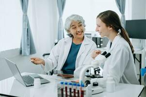 Two scientist or medical technician working, having a medical discuss meeting with an Asian senior female scientist supervisor in the laboratory with online reading, test samples and innovation photo