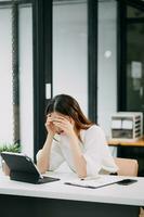 Asian business woman is stressed, bored, and overthinking from working on a tablet at the modern office. photo