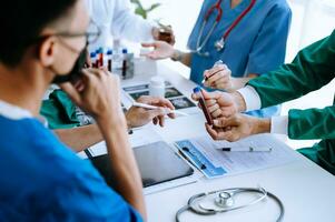 Medical team having a meeting with doctors in white lab coats and surgical scrubs seated at a table discussing a patients working online using computers photo