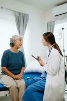 Friendly Female Head Nurse Making Rounds does Checkup on Patient Resting in Bed. She Checks tablet while Man Fully Recovering after Successful Surgery in hospital photo