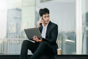 Young Asian business man working at outside business center with laptop, tablet, smartphone and taking notes on the paper. photo