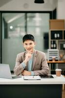 Young handsome man typing on tablet and laptop while sitting at the working wooden table modern office room photo